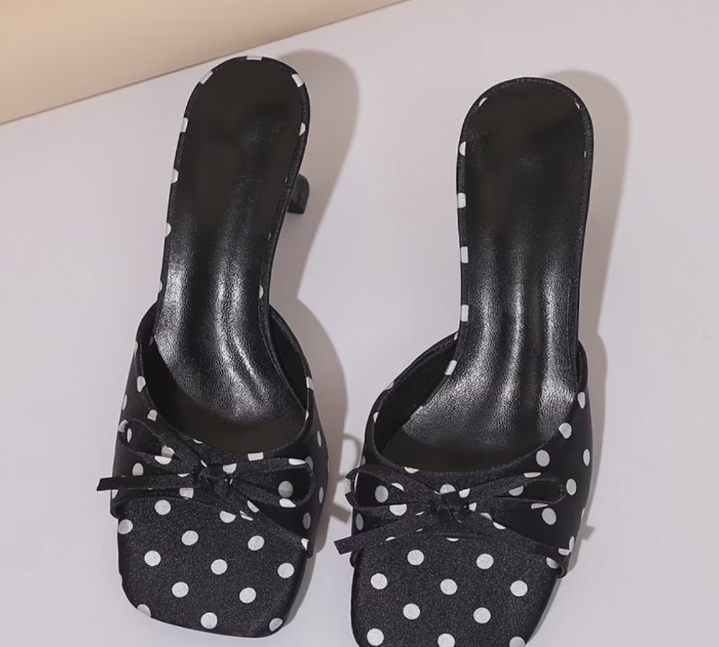 Une paire de sandales noires à pois pour femme avec texture satinée et décoration de nœud. Dotées d'une pointe carrée, d'un dos ouvert et d'un talon aiguille, ces pantoufles polyvalentes et élégantes sont antidérapantes, résistantes à l'usure et d'un styl